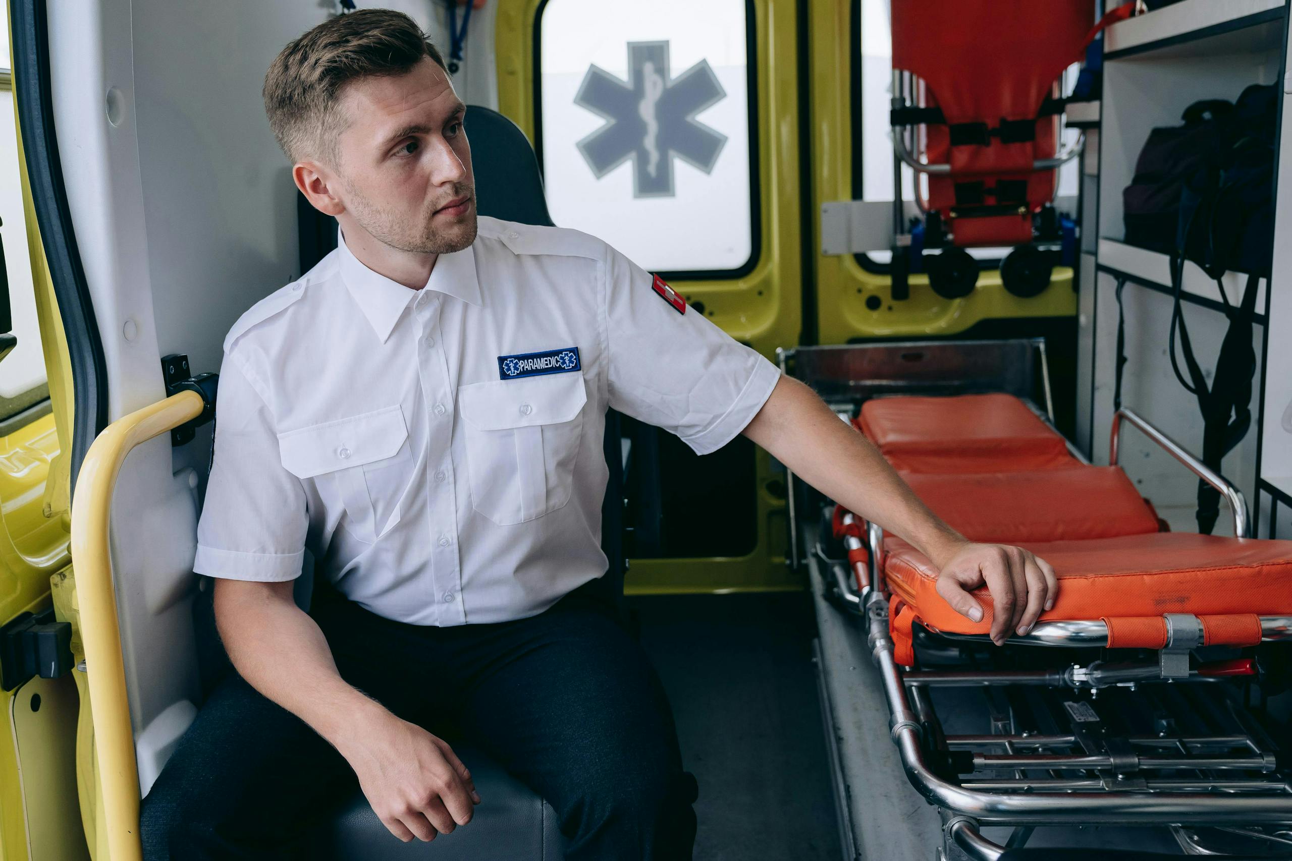 A paramedic seated inside an ambulance next to an empty gurney.